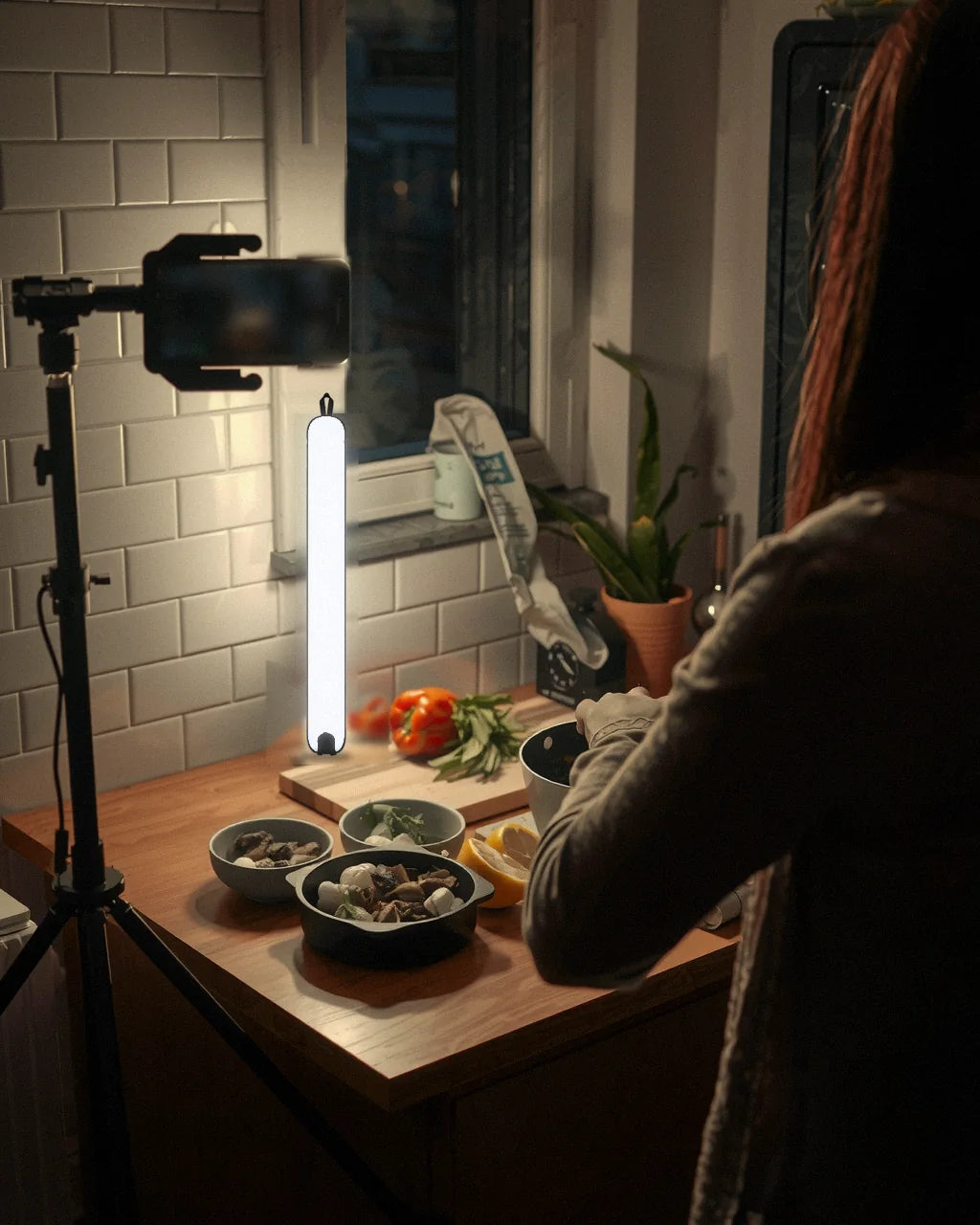 Hands slicing a red pepper on a chopping board, lit by a Creator Lamp standing on the counter while a phone on a tripod films