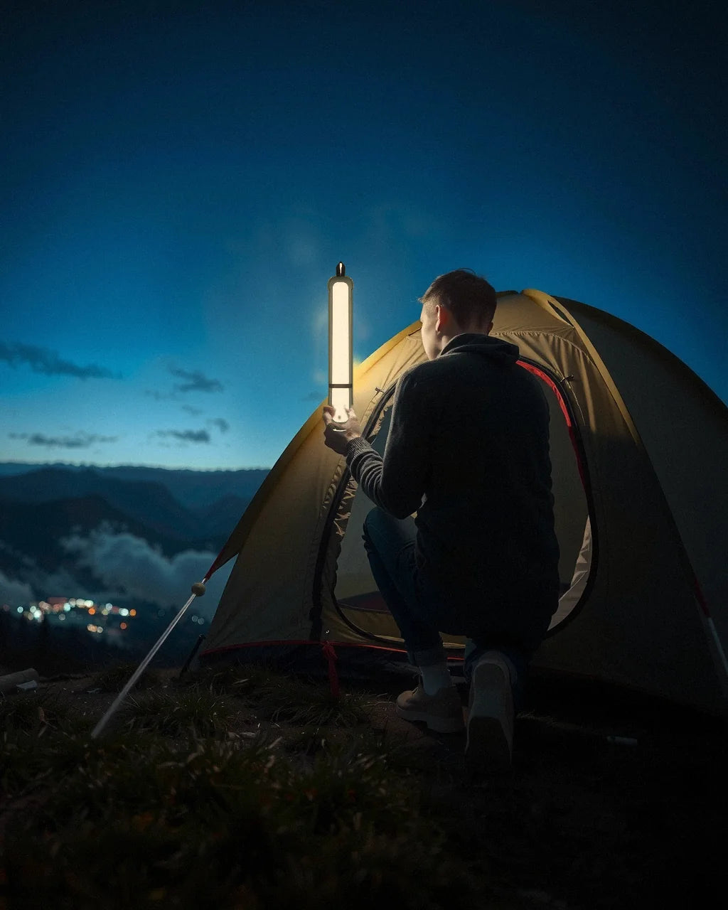 Someone kneeling by a tent at dusk, holding up an Adventure Lamp by its base