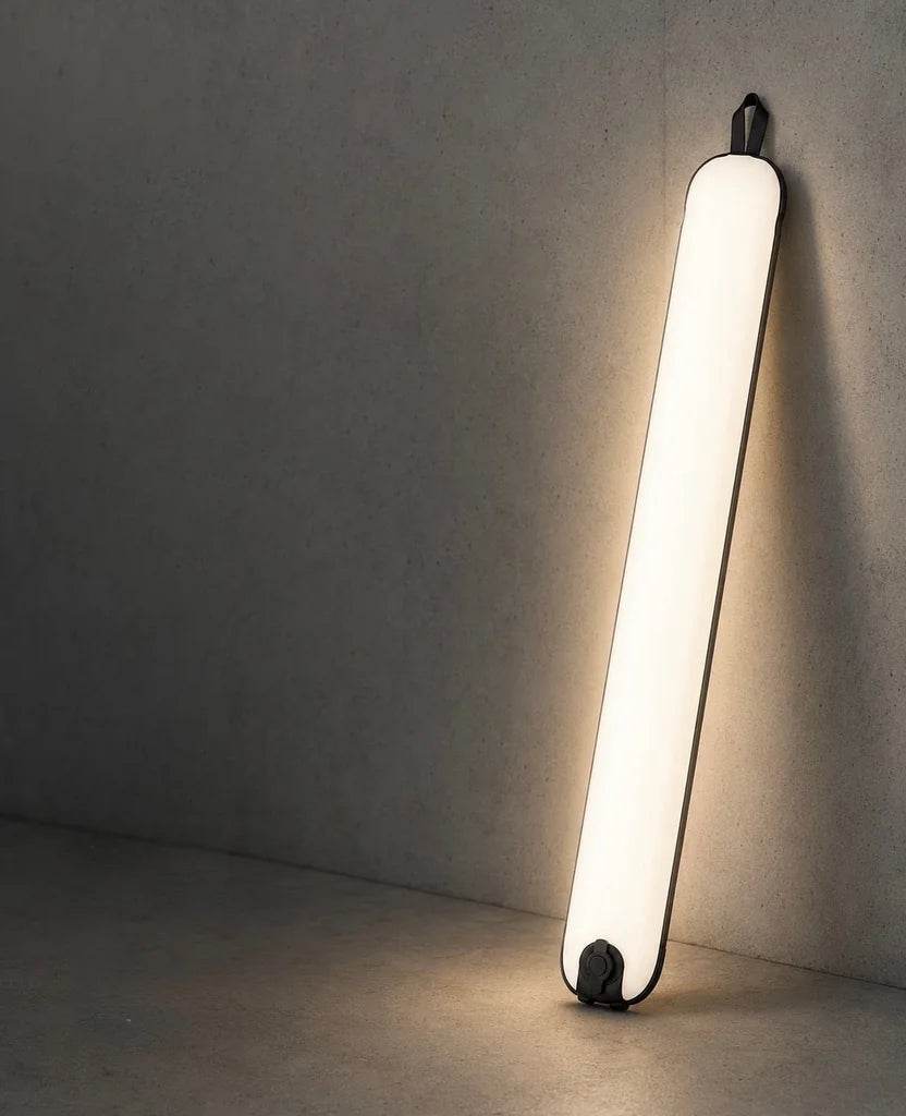 The Creator Lamp lit in warm white, leaning against a concrete wall